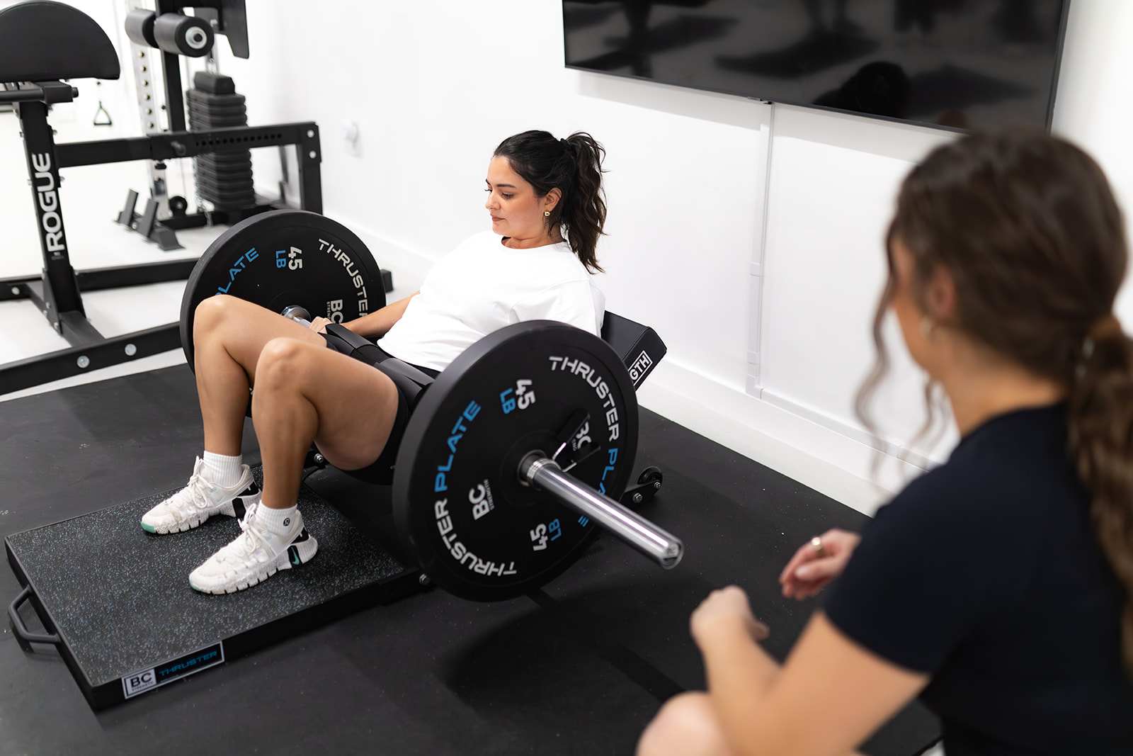 Client performing a weighted hip thrust while her trainer coaches