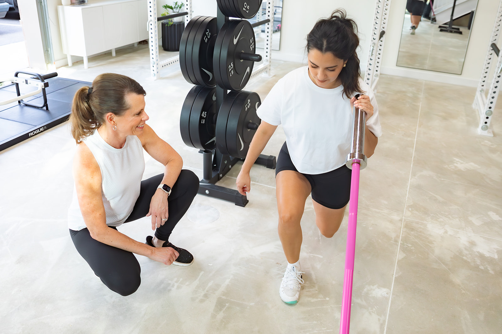 Coach guiding a client setting up for a lift with a pink barbell
